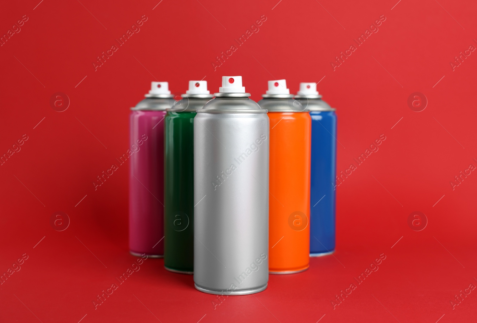 Photo of Colorful cans of spray paints on red background