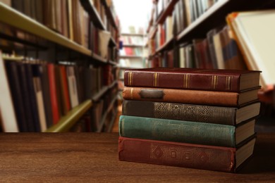 Many stacked hardcover books on wooden table in library, space for text