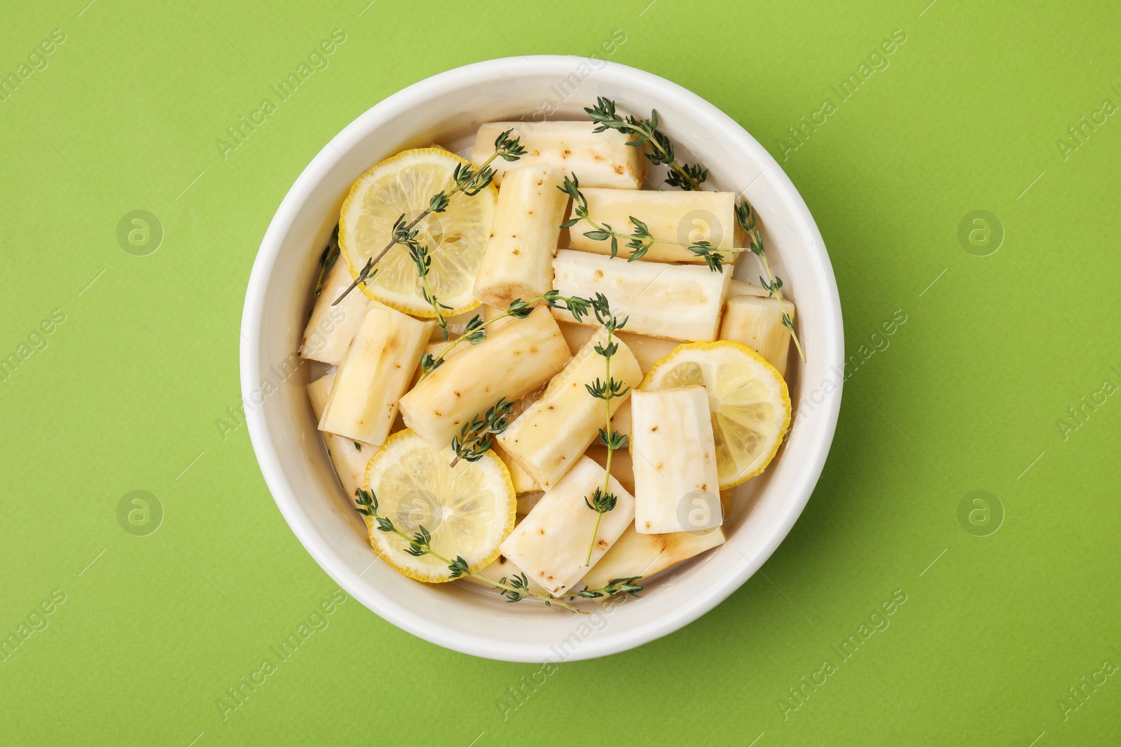 Photo of Dish with raw salsify roots, lemon and thyme on green table, top view