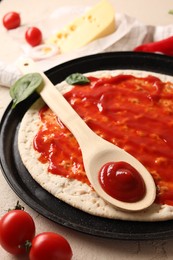 Photo of Pizza base smeared with sauce and tomatoes on light textured table, closeup