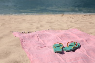Photo of Pink striped beach towel and flip flops on sandy seashore