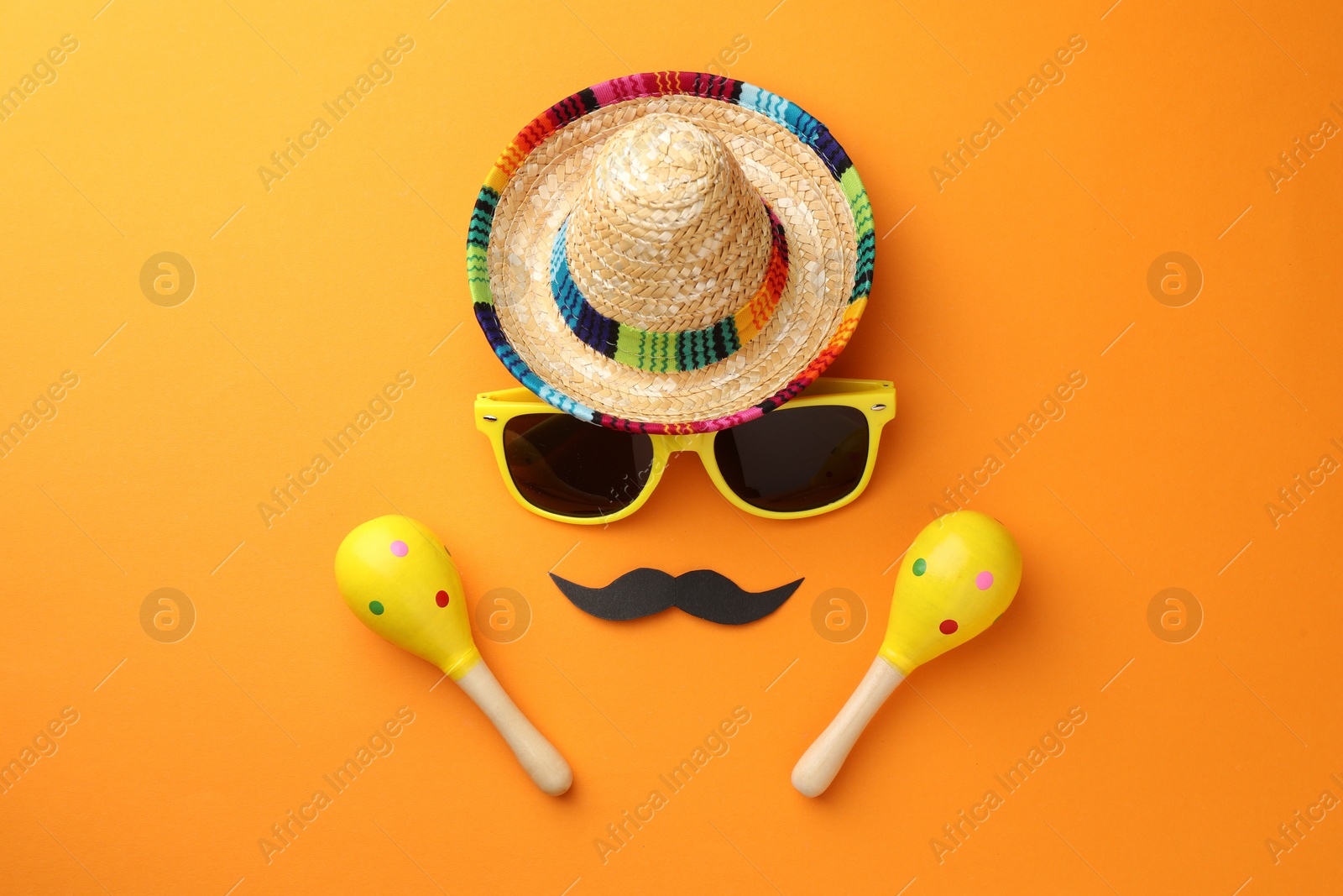 Photo of Mexican sombrero hat, sunglasses, fake mustache and maracas on orange background, flat lay