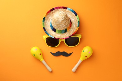 Mexican sombrero hat, sunglasses, fake mustache and maracas on orange background, flat lay