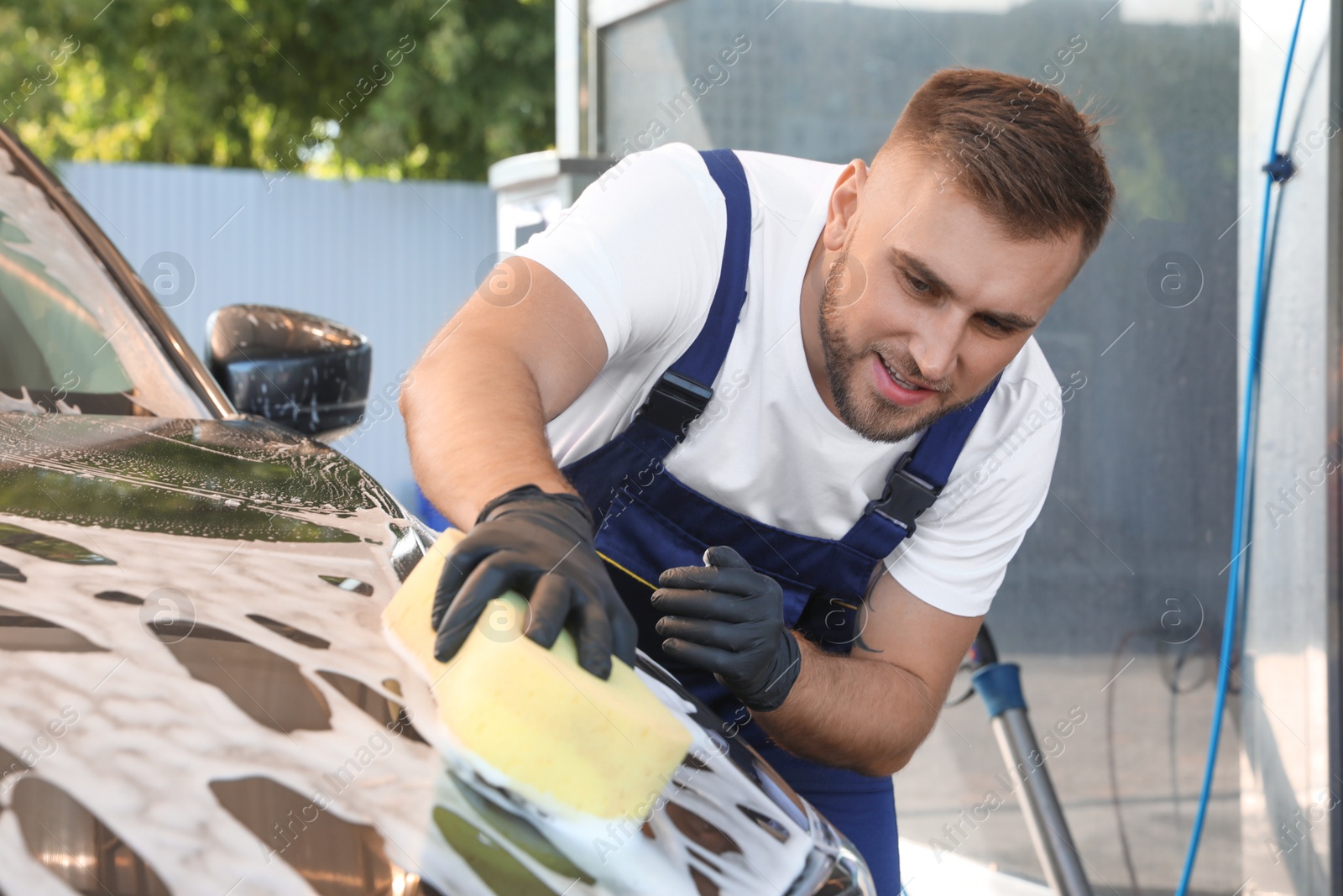 Photo of Young worker cleaning automobile with sponge at car wash