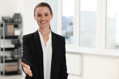 Happy woman welcoming and offering handshake in office, space for text