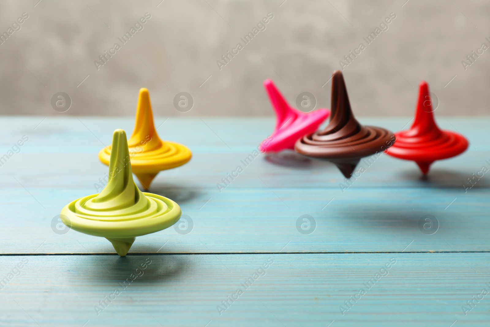 Photo of Bright spinning tops on light blue wooden table, closeup