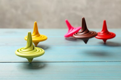 Photo of Bright spinning tops on light blue wooden table, closeup