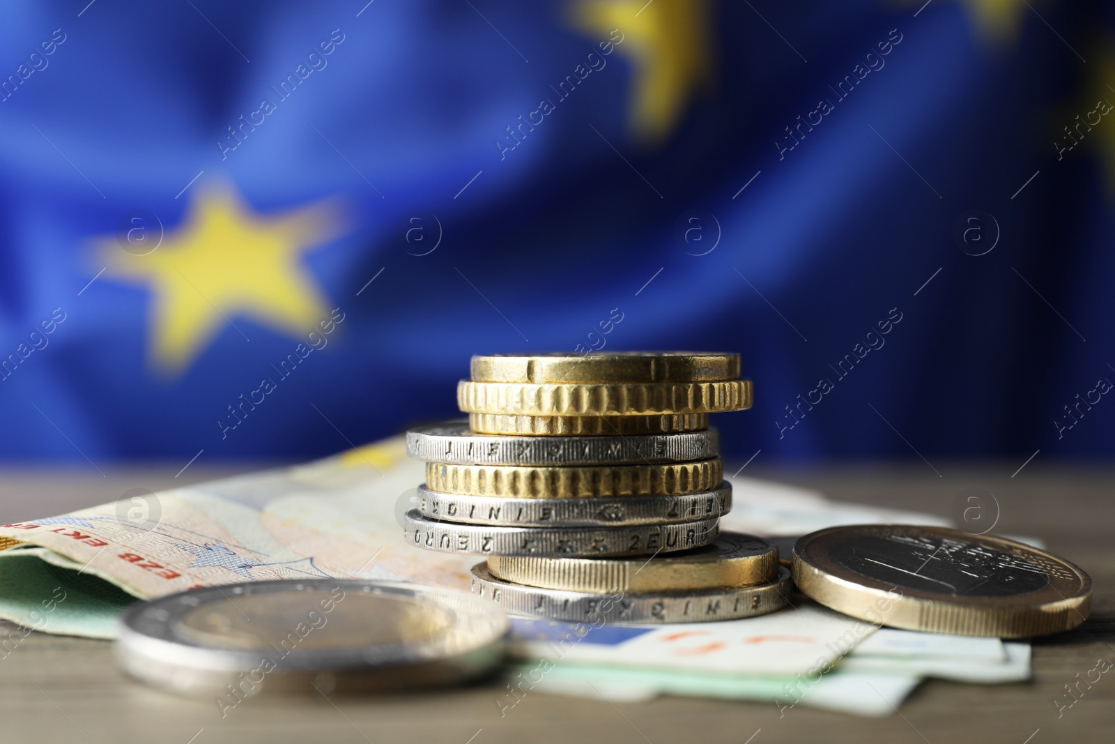 Photo of Coins and banknotes on wooden table against European Union flag, space for text