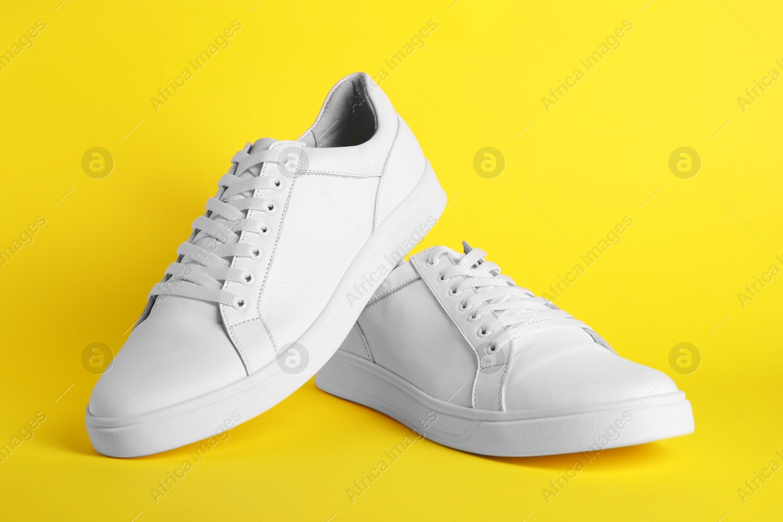 Photo of Pair of stylish white sneakers on yellow background