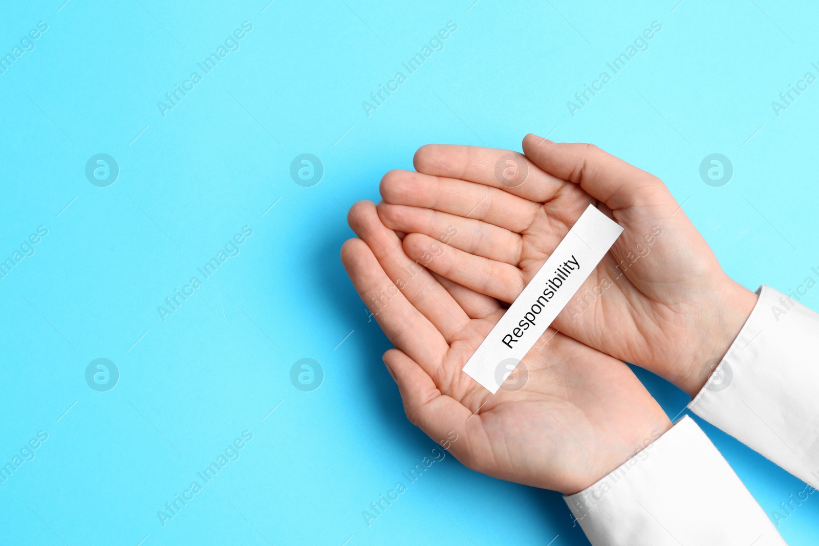 Photo of Woman holding paper with word Responsibility on light blue background, top view. Space for text