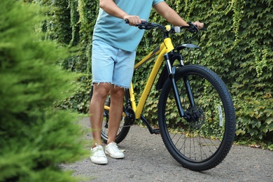Photo of Young man with bicycle near wall covered with green ivy vines on city street, closeup