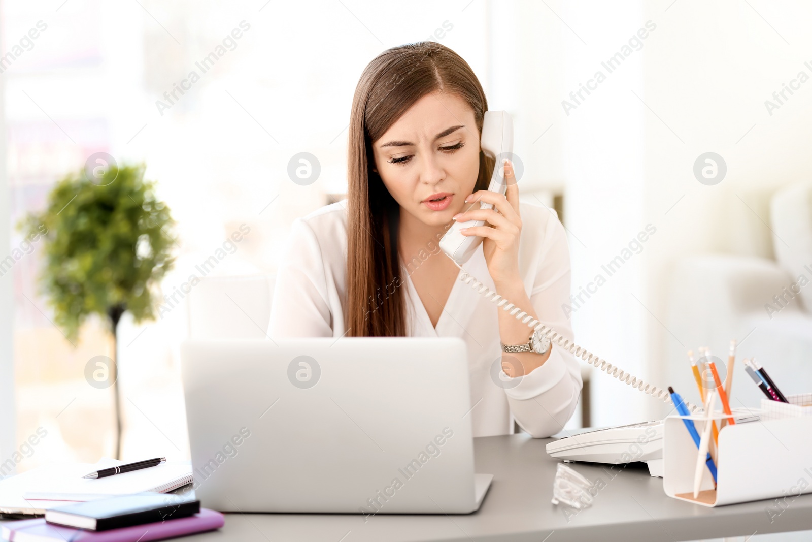 Photo of Young woman talking on phone at workplace