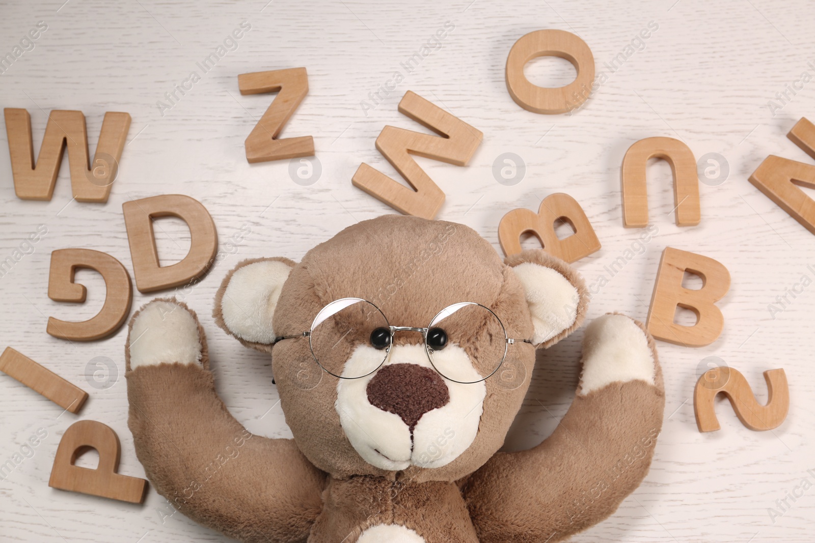 Photo of Dyslexia concept. Teddy bear with glasses and letters on light wooden table, flat lay