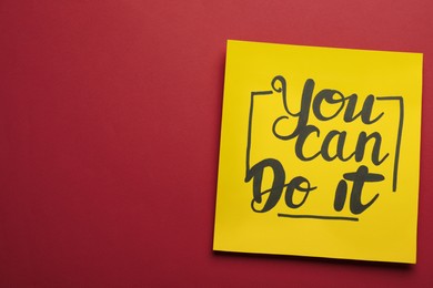 Photo of Yellow card with motivational phrase You Can Do It on burgundy background, top view. Space for text