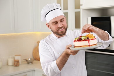 Photo of Happy professional confectioner decorating delicious cake in kitchen