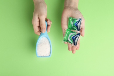 Woman holding laundry capsules and detergent powder on green background, top view