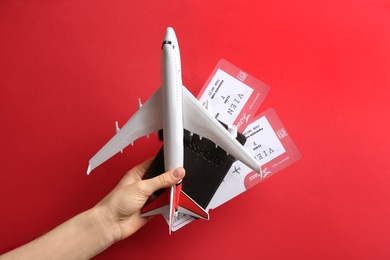 Woman holding toy airplane, passport and tickets on red background, closeup