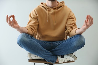 Man meditating in office chair against light background, closeup