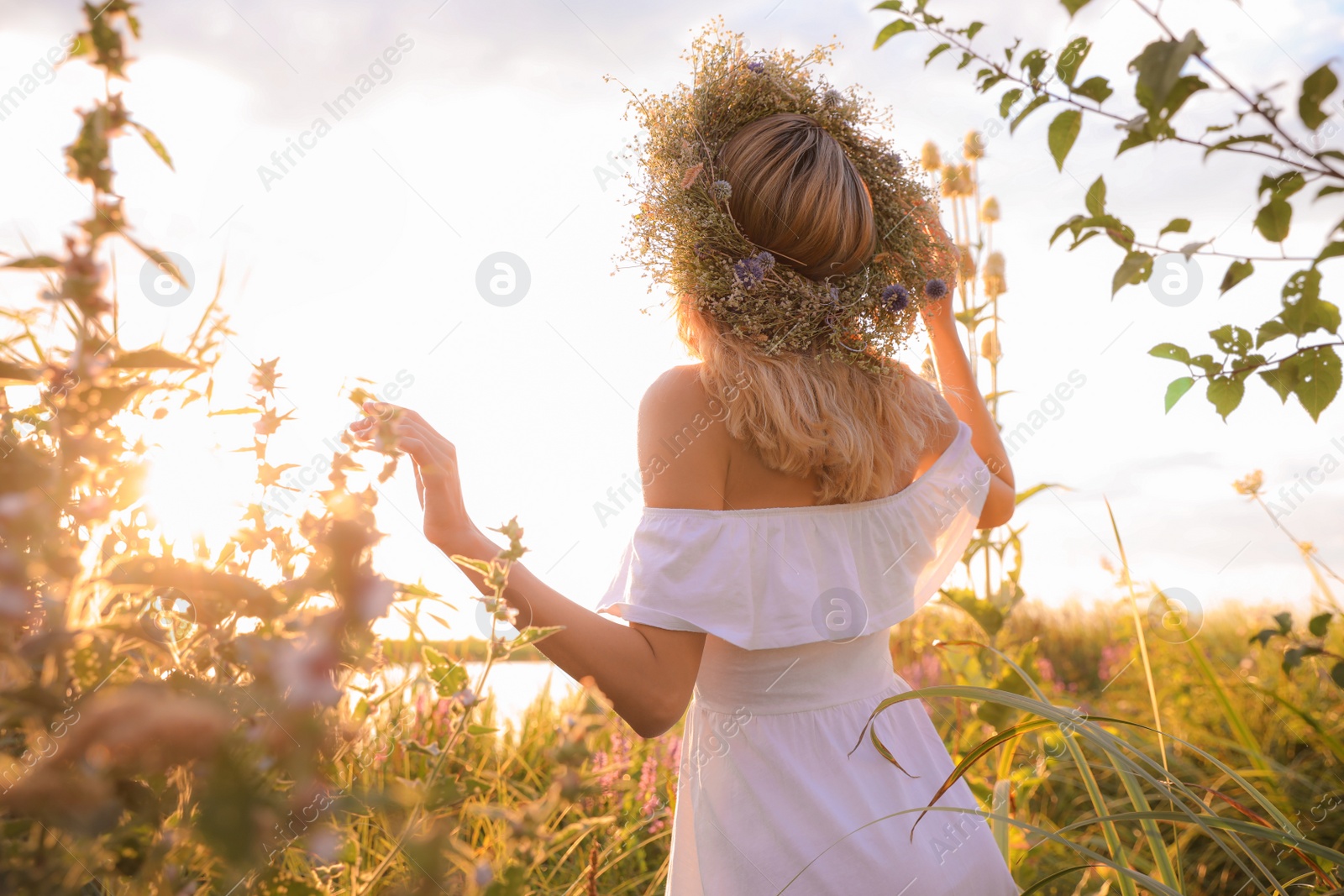 Photo of Young woman wearing wreath made of beautiful flowers outdoors on sunny day