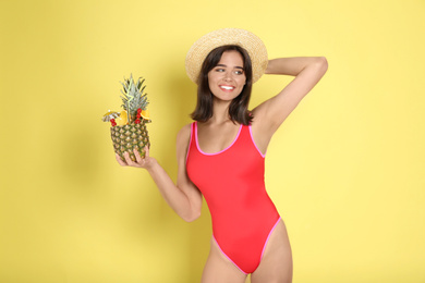 Beautiful woman in red swimsuit holding tropical cocktail on yellow background
