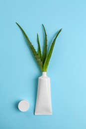 Photo of Tube of toothpaste and fresh aloe on light blue background, flat lay