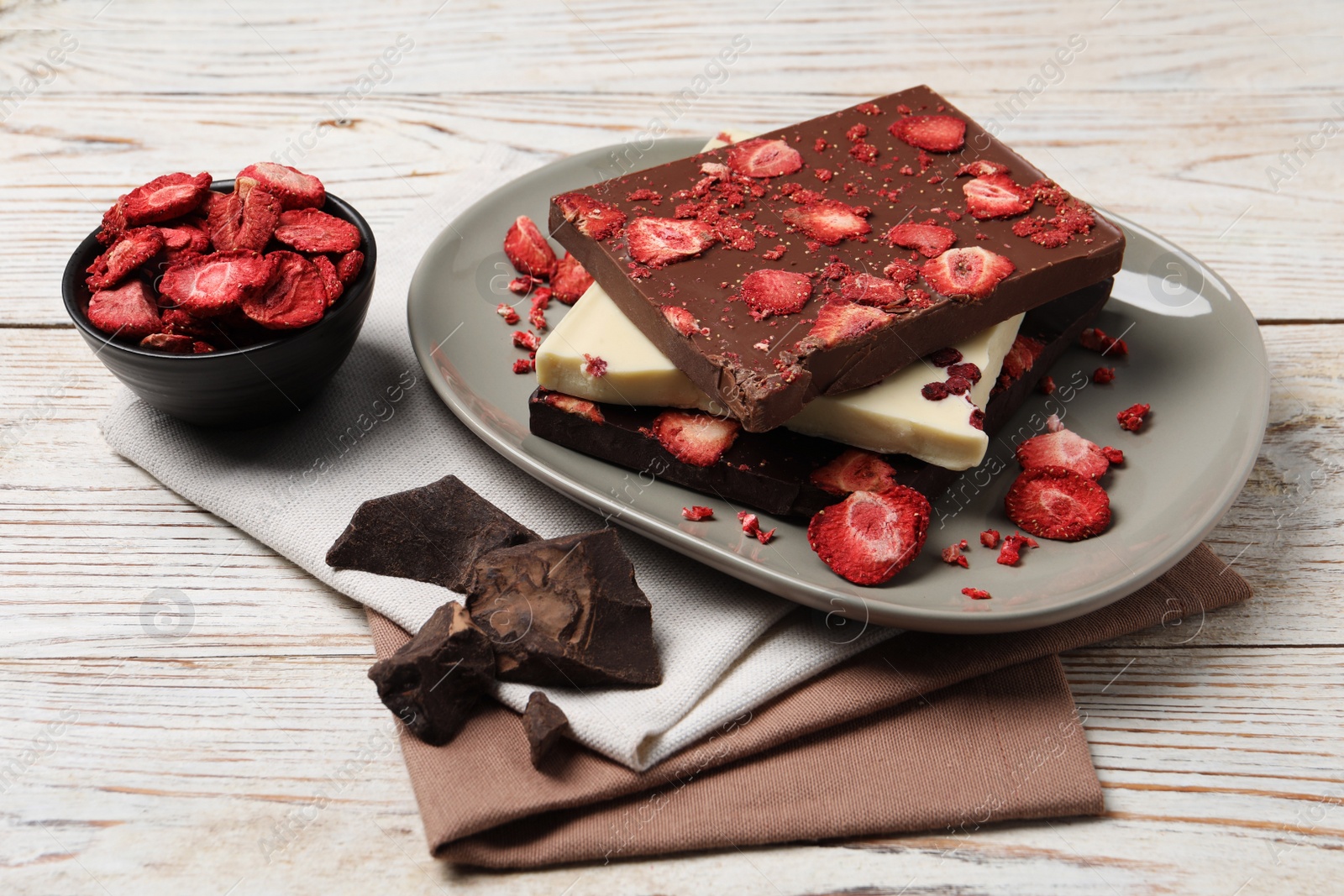 Photo of Plate and different chocolate bars with freeze dried fruits on white wooden table