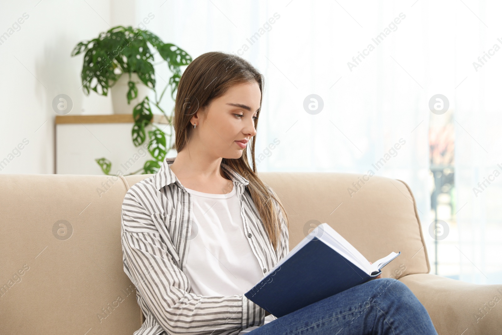 Photo of Young woman reading book on sofa at home