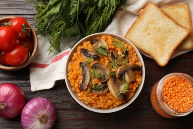 Photo of Delicious red lentils with mushrooms and dill in bowl served on wooden table, flat lay