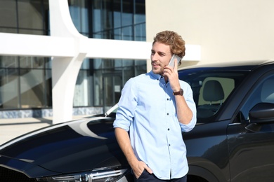 Photo of Young man talking on phone near modern car, outdoors