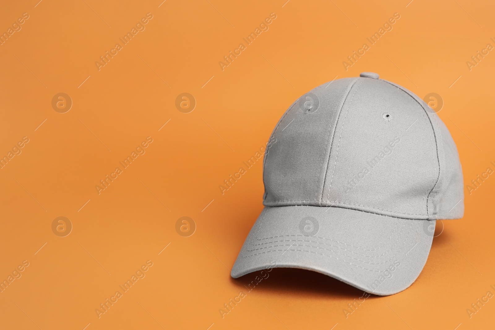 Photo of Stylish grey baseball cap on orange background. Space for text