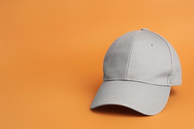 Photo of Stylish grey baseball cap on orange background. Space for text