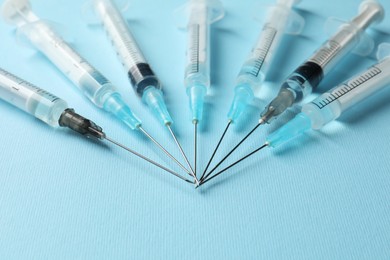 Disposable syringes with needles and medicine on light blue background