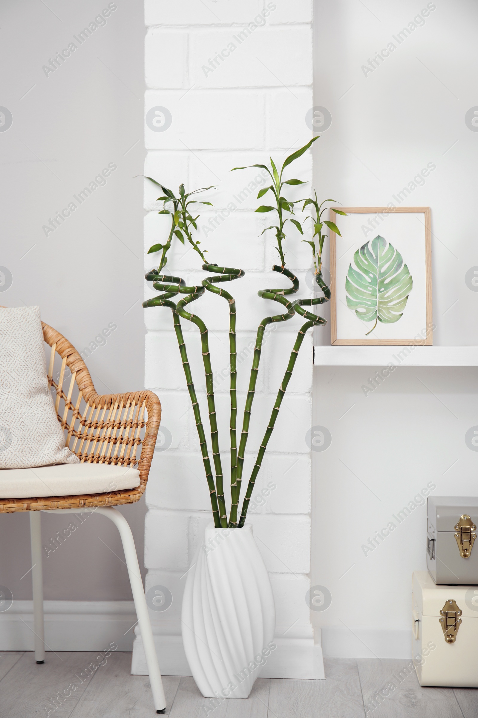 Photo of Vase with green bamboo stems on floor in room. Interior design