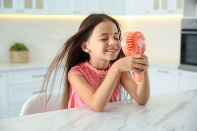 Little girl enjoying air flow from portable fan at home. Summer heat