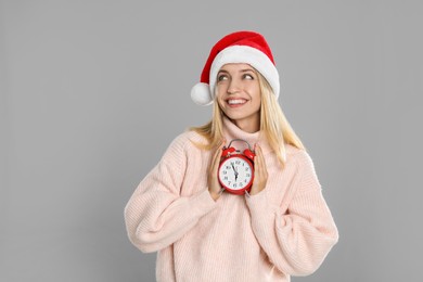 Woman in Santa hat with alarm clock on grey background. New Year countdown