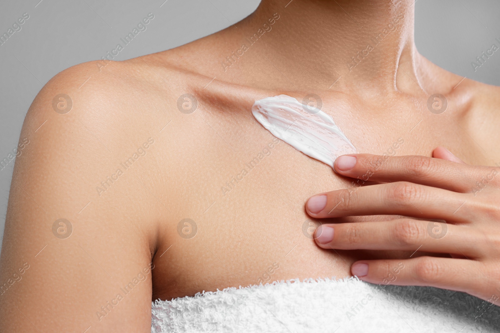 Photo of Woman applying cream onto body on grey background, closeup