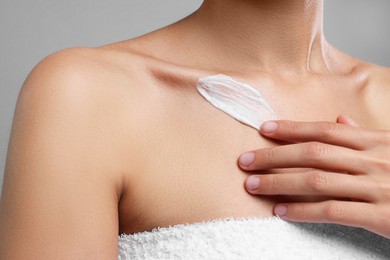 Woman applying cream onto body on grey background, closeup