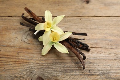 Aromatic vanilla sticks and flowers on wooden table, closeup