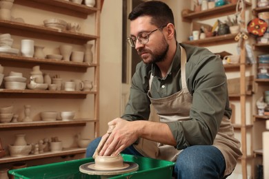 Photo of Clay crafting. Man making bowl on potter's wheel in workshop, space for text