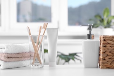 Photo of Bamboo toothbrushes in holder, cosmetic product and towels on white table indoors