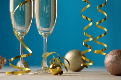 Photo of Glasses of champagne with serpentine streamers and Christmas ornaments on table against blue background, closeup