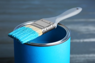 Paint can and dipped brush on wooden background, closeup