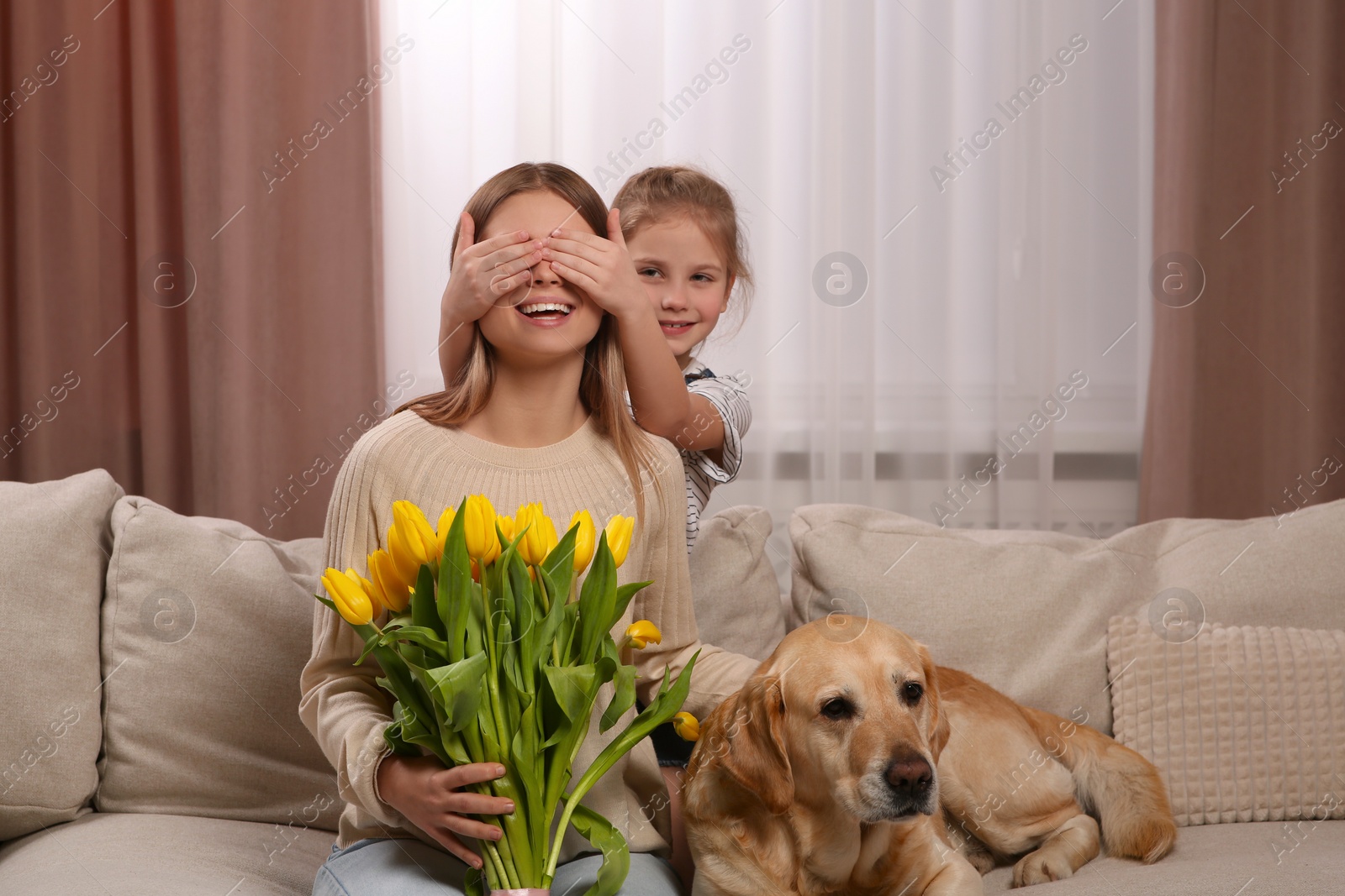 Photo of Little daughter congratulating mom with bouquet of yellow tulips at home. Happy Mother's Day