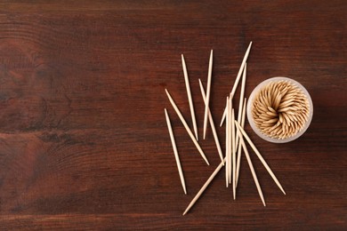 Disposable toothpicks and holder on wooden background, flat lay. Space for text