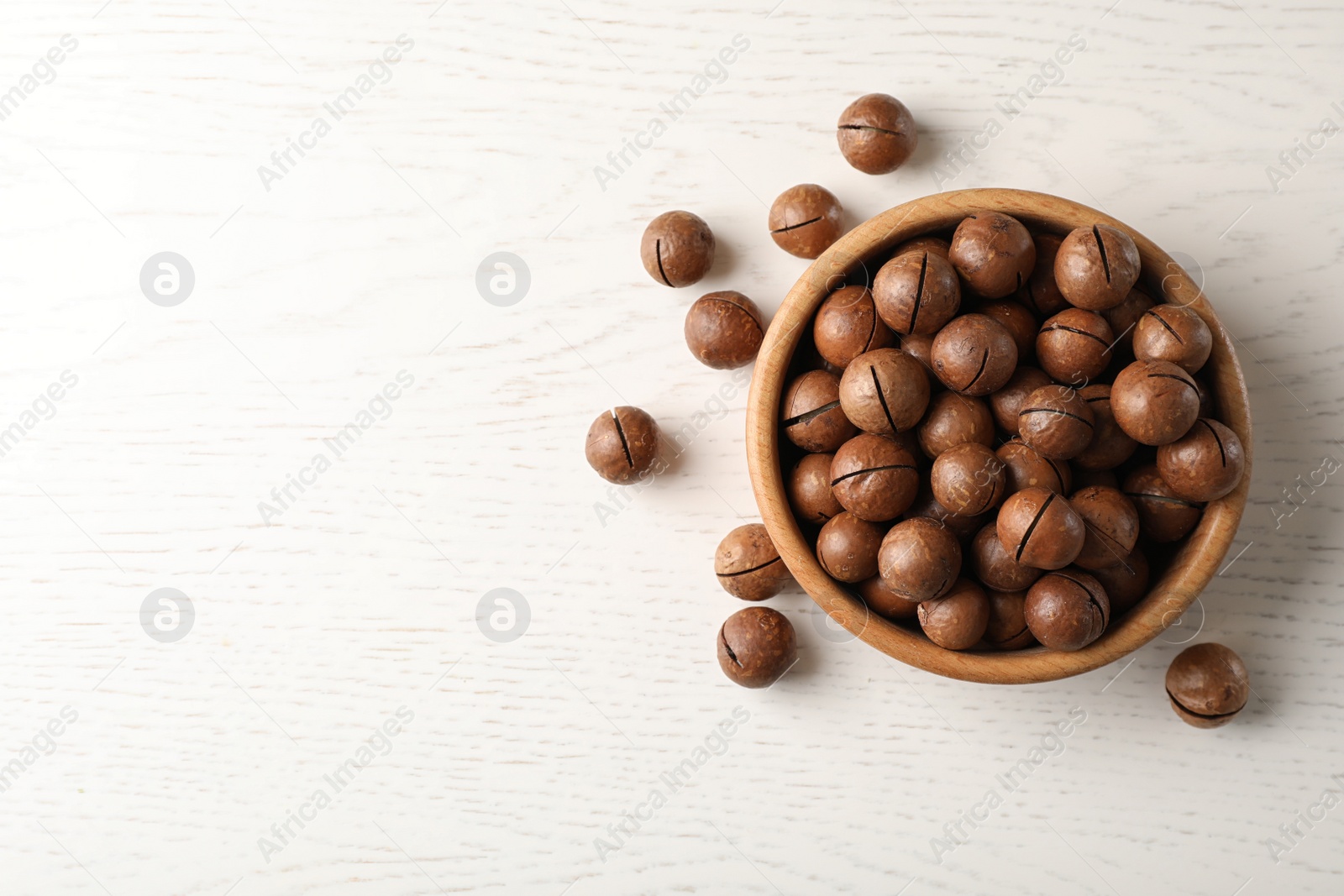 Photo of Bowl with organic Macadamia nuts on wooden table, top view. Space for text