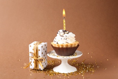 Delicious birthday cupcake with candle and gift box on brown background