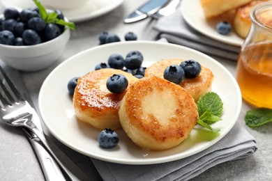 Photo of Delicious cottage cheese pancakes with blueberries, mint and honey on light grey table, closeup