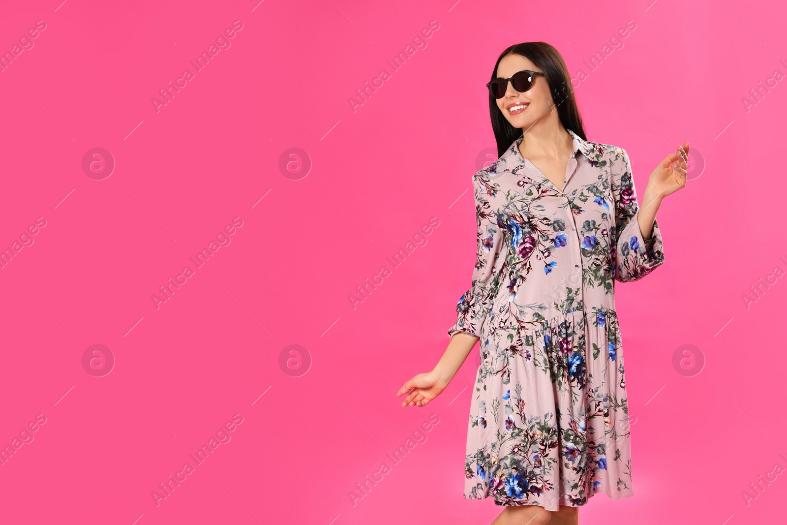 Photo of Young woman wearing floral print dress and sunglasses on pink background. Space for text