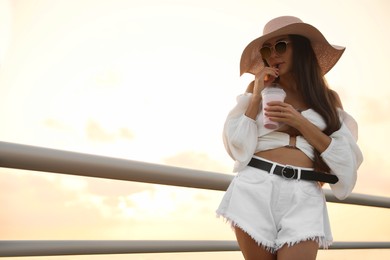 Photo of Beautiful young woman with tasty milk shake outdoors, space for text