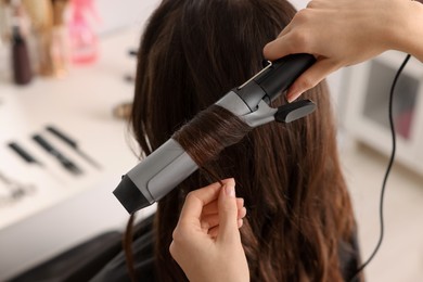 Photo of Hairdresser working with client using curling hair iron in salon, closeup